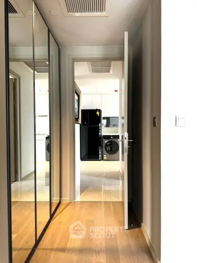 Modern hallway with mirrored closet doors leading to a sleek kitchen with appliances.