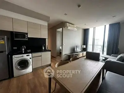 Modern living room with open kitchen, featuring sleek appliances and large windows.