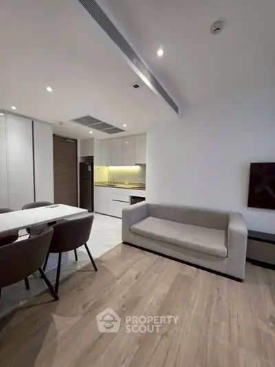 Modern open-plan living room with sleek kitchen and dining area, featuring contemporary furniture and wooden flooring.