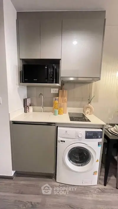 Modern compact kitchen with washing machine and microwave in sleek cabinetry.