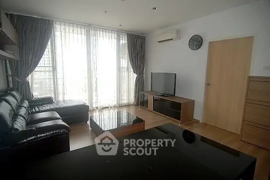 Modern living room with leather sofa, TV, and large windows offering natural light.