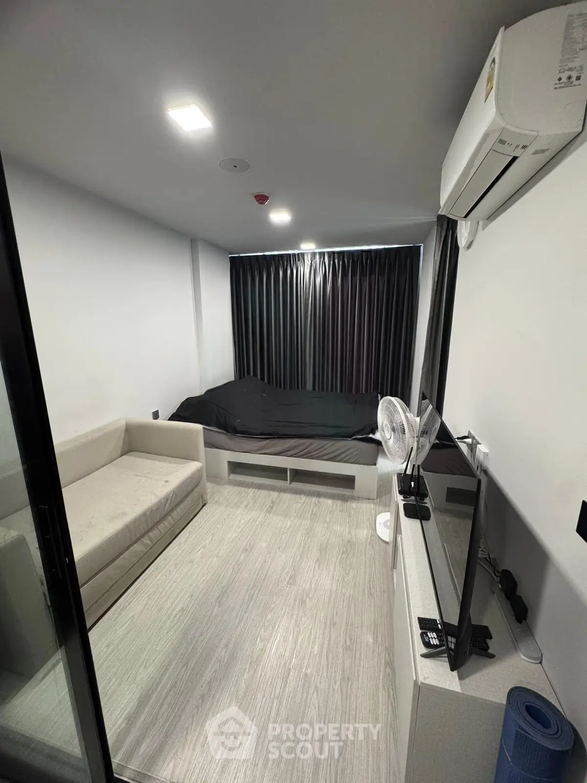 Modern compact living room with sofa, bed, and TV, featuring sleek design and efficient use of space.