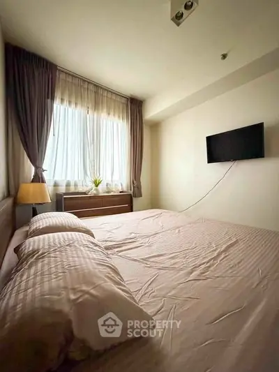 Cozy bedroom with natural light and wall-mounted TV, perfect for relaxation.