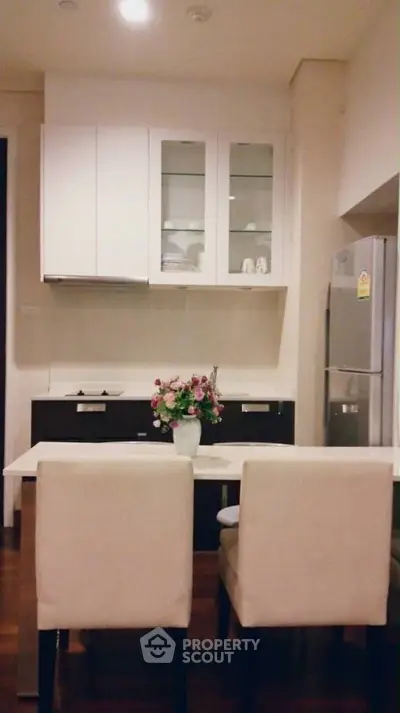 Modern kitchen with sleek cabinets and dining area, featuring a stylish fridge and elegant decor.