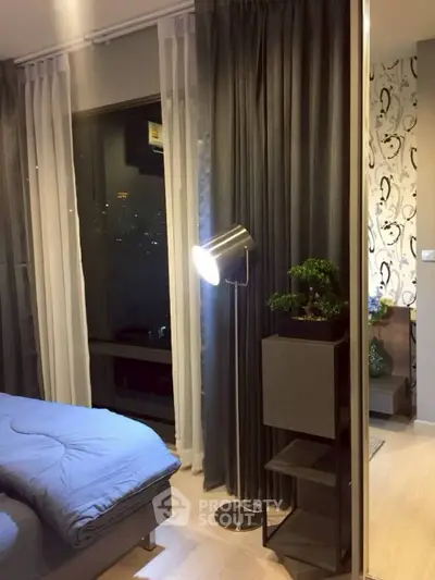 Modern bedroom with stylish lighting and city view, featuring elegant curtains and cozy bedding.