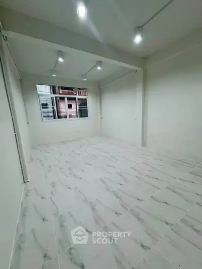 Spacious unfurnished room with marble flooring and large window, ideal for customization.