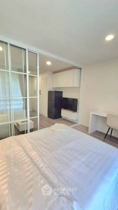 Modern bedroom with glass partition, sleek furniture, and natural light in a stylish apartment.
