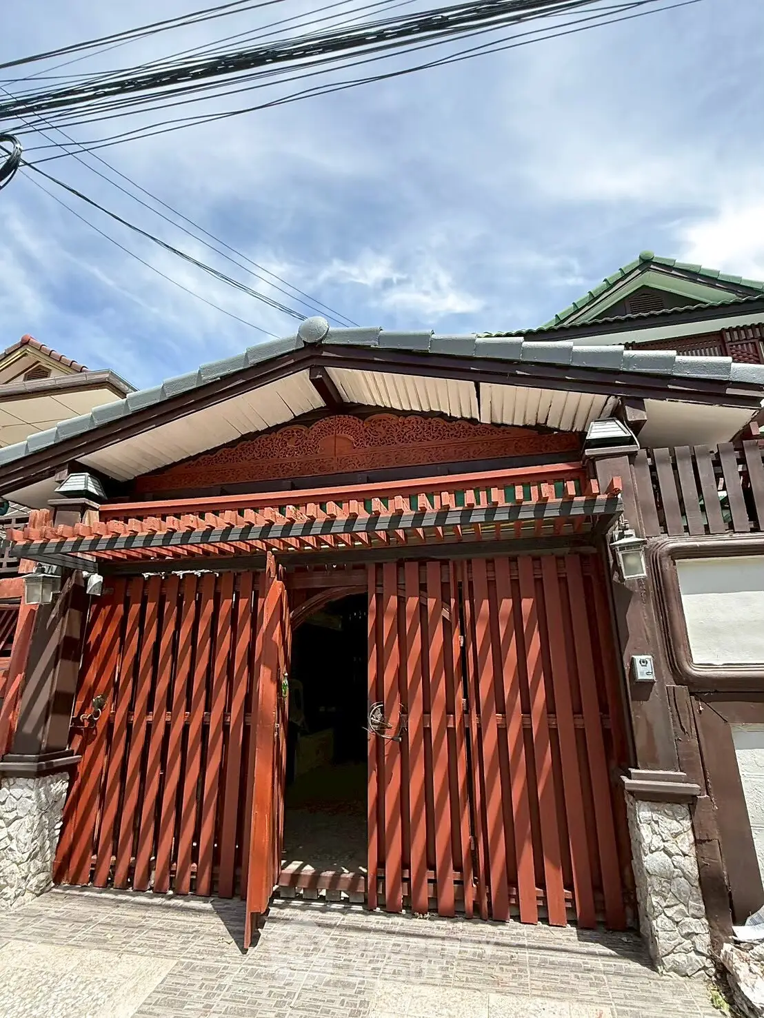 Charming traditional house entrance with wooden gate and tiled roof under a clear blue sky.