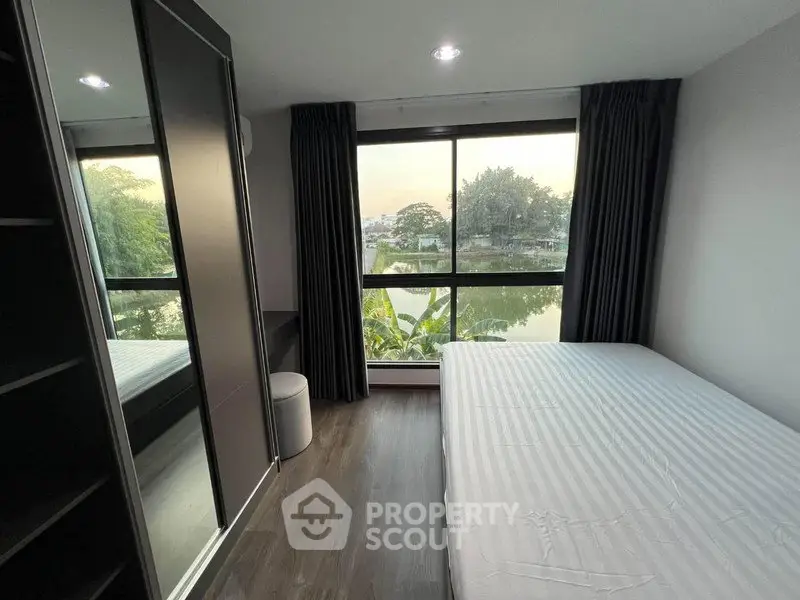 Modern bedroom with large window offering serene water view and sleek furnishings.