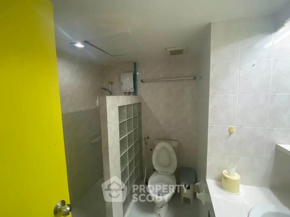 Compact bathroom with shower and toilet, featuring a bright yellow door for a modern touch.