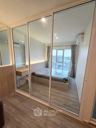 Modern bedroom with mirrored closet and city view, featuring sleek design and natural light.