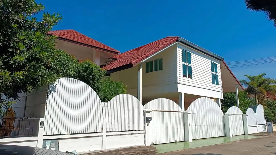Charming white house with red roof and unique fence design under clear blue sky.