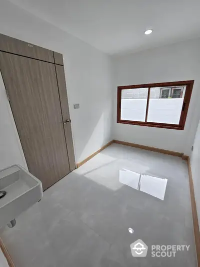 Pristine modern bathroom with sleek finishes, featuring a wall-mounted sink, large window for natural light, and a wooden door for a touch of warmth.