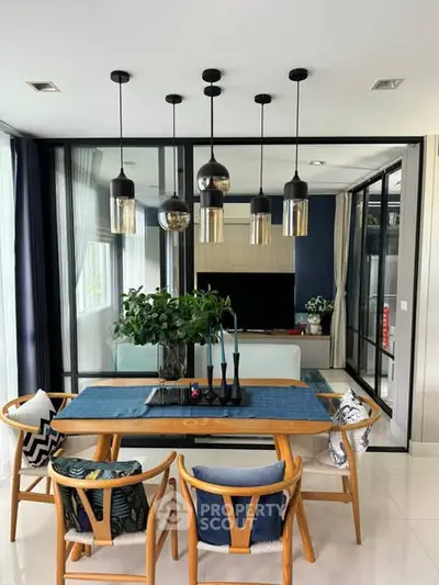 Modern dining area with stylish pendant lights and glass partition leading to a cozy living room.