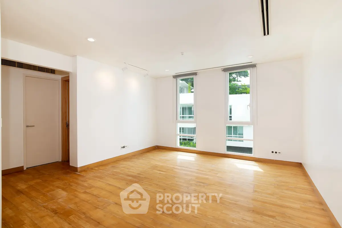 Spacious empty room with wooden flooring and large windows in modern apartment