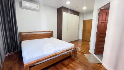 Spacious bedroom with wooden flooring and modern wardrobe in a cozy apartment.