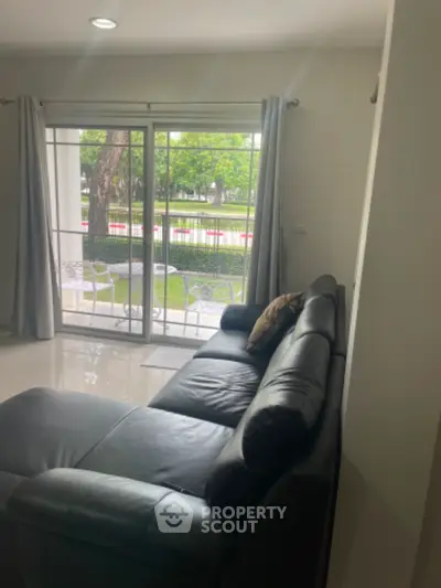 Spacious living room with leather sofa and garden view through large windows.