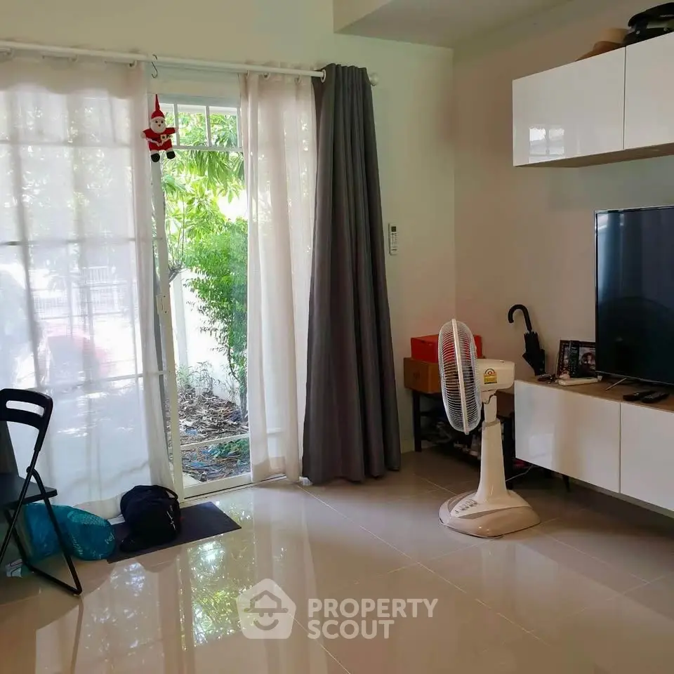 Cozy living room with modern decor and garden view, featuring sleek TV setup and natural light.