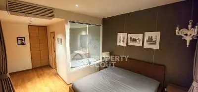 Modern bedroom with glass wall view into luxurious bathroom featuring bathtub and elegant decor.