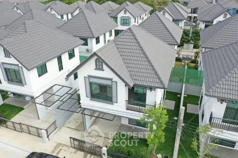 Aerial view of a modern residential neighborhood showcasing a collection of elegant white houses with grey tiled roofs, manicured lawns, and driveways, reflecting a serene suburban lifestyle.