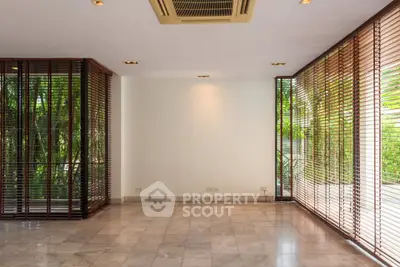 Spacious living room with large windows and marble flooring, offering a serene garden view.