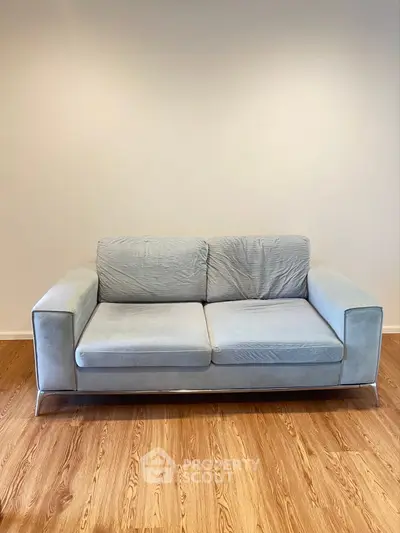 Modern blue sofa on wooden floor in minimalist living room setting.