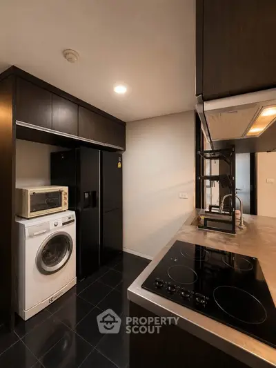 Modern kitchen with sleek appliances and dark cabinetry, featuring a washing machine and microwave.