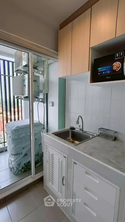 Modern compact kitchen with balcony view, featuring sleek cabinetry and built-in microwave, perfect for urban living.