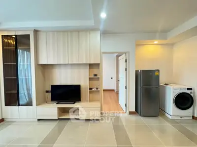 Modern living room with sleek wooden cabinetry, TV, fridge, and washing machine in a bright apartment.