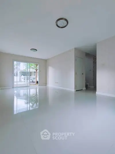 Spacious empty living room with glossy white tiles and large window view.