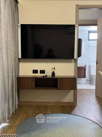 Modern living room with wall-mounted TV and sleek wooden cabinet, adjacent to a bathroom entrance.