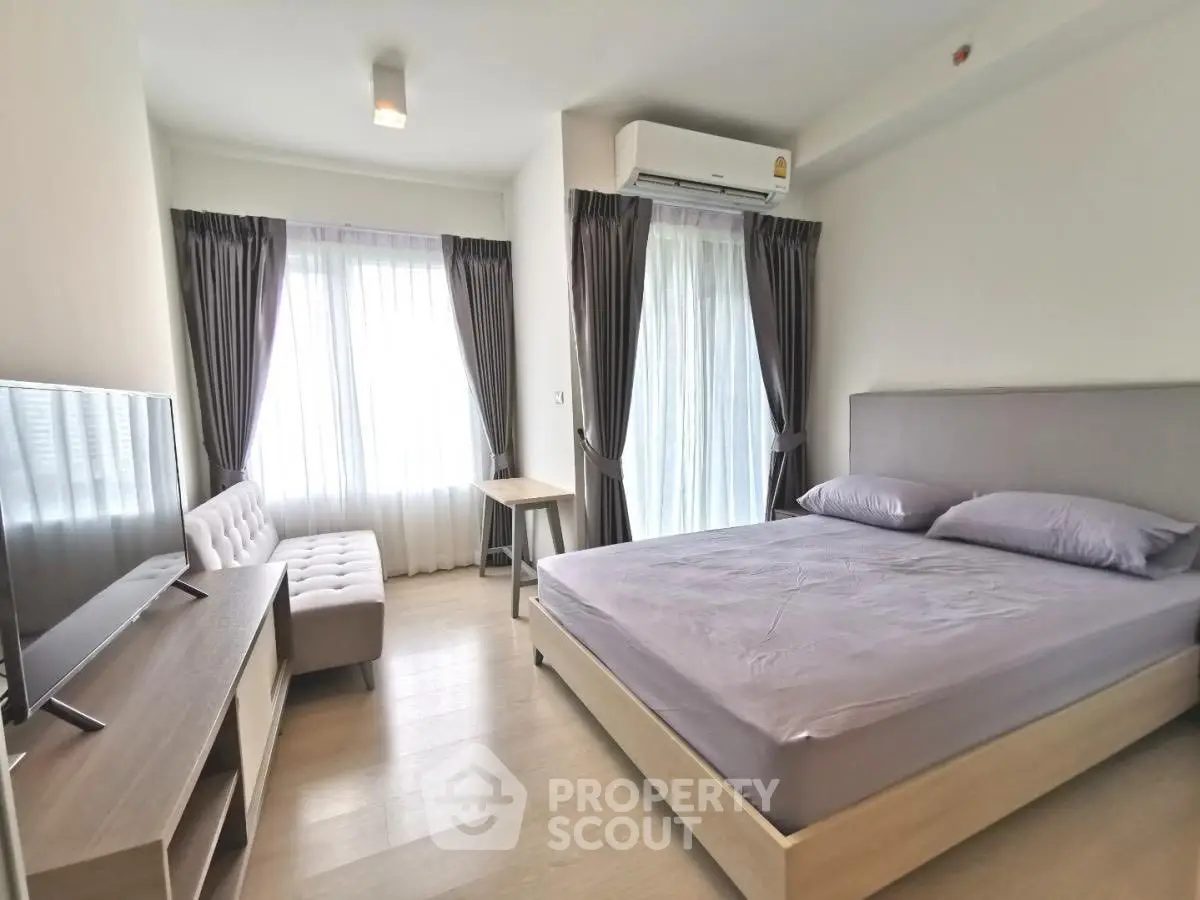 Modern bedroom with natural light, featuring a cozy bed, TV, and stylish sofa.