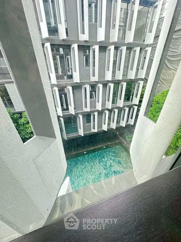 Modern building exterior with unique window design overlooking a serene pool area.