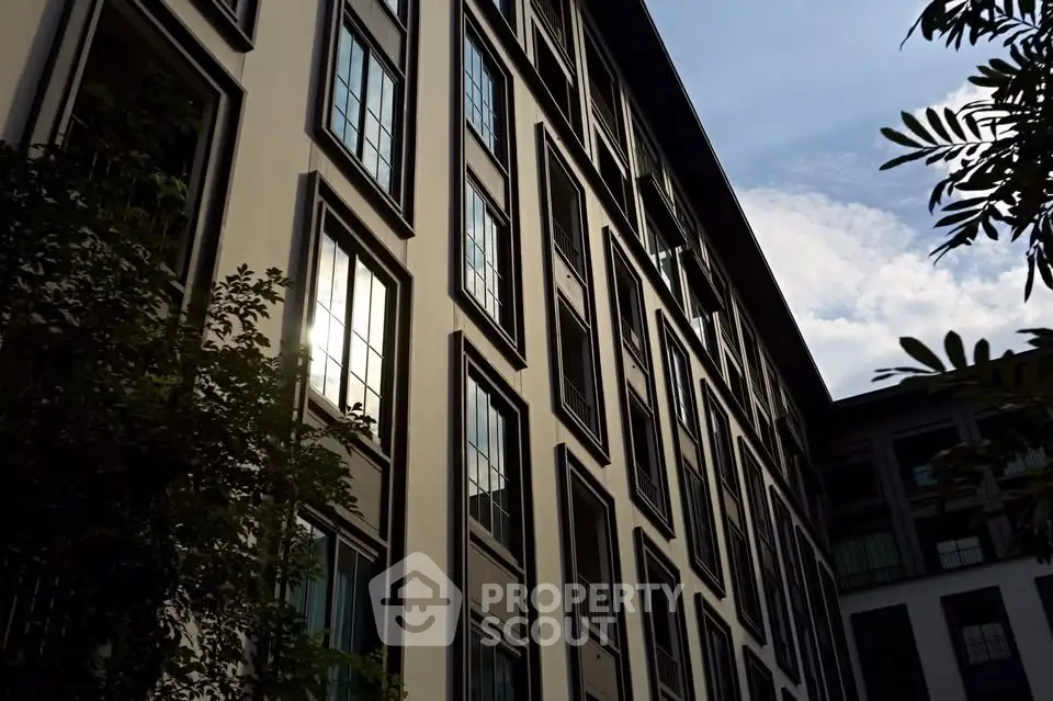 Modern apartment building exterior with large windows and lush greenery.