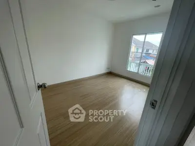 Spacious empty bedroom with wooden flooring and large window offering natural light.