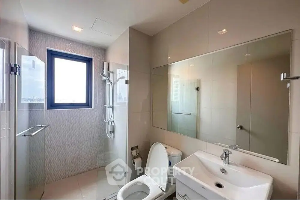 Modern bathroom with sleek fixtures and large mirror, featuring a shower and window view.