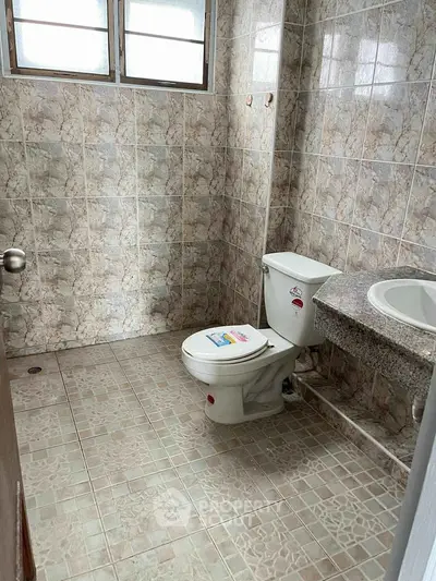 Spacious bathroom with tiled walls and floor, featuring a toilet and sink.