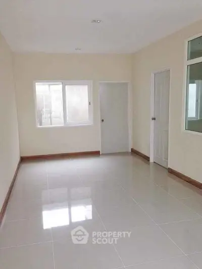 Spacious empty room with glossy tiled floor and large windows for natural light.