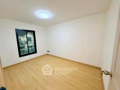 Spacious empty room with wooden flooring and large window in modern apartment.