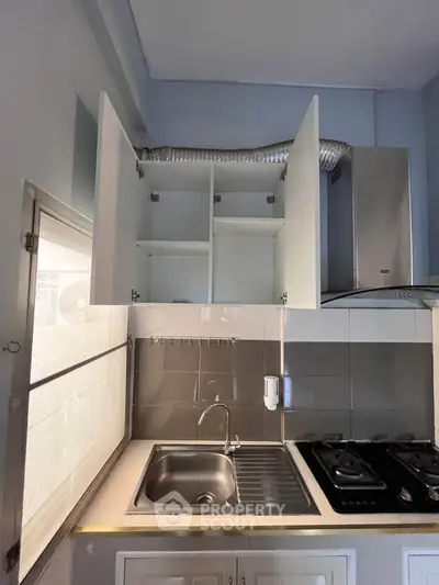 Compact kitchen with gas stove and overhead cabinets in modern apartment