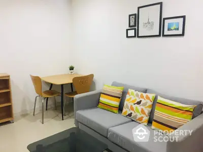 Cozy modern living room with a comfortable grey sofa adorned with vibrant cushions, a neat dining area, and tasteful wall art, perfect for urban living.