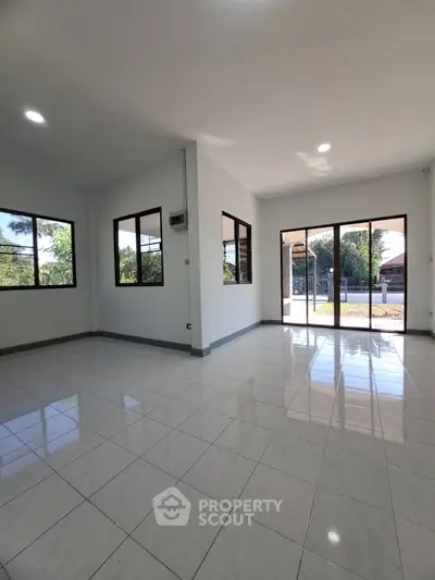 Spacious sunlit living room with large windows and glossy tiled floors, perfect for modern living.