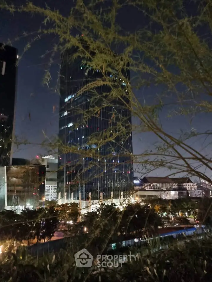 Stunning night view of a modern skyscraper with city lights and lush greenery in the foreground.