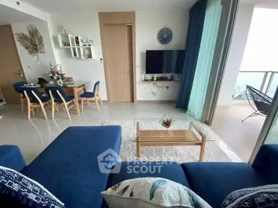 Modern living room with blue sofa, wall-mounted TV, and balcony with ocean view.