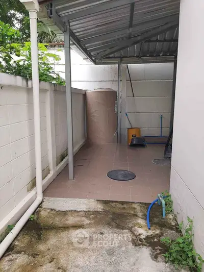 Outdoor utility area with covered roof and water tank, ideal for storage or laundry setup.