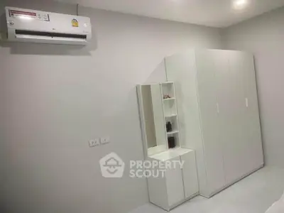 Modern bedroom with sleek white wardrobe and air conditioning unit, perfect for minimalist living.