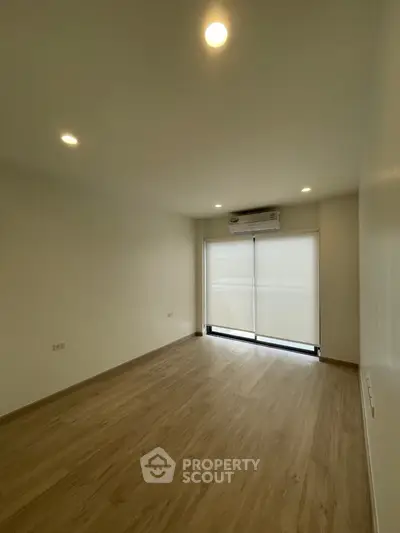 Spacious empty room with wooden flooring and large window, perfect for customization.