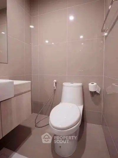 Modern bathroom with sleek fixtures and neutral tiles, featuring a toilet and vanity.