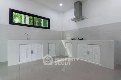Modern kitchen with sleek white cabinets and gas stove, featuring a large window for natural light.