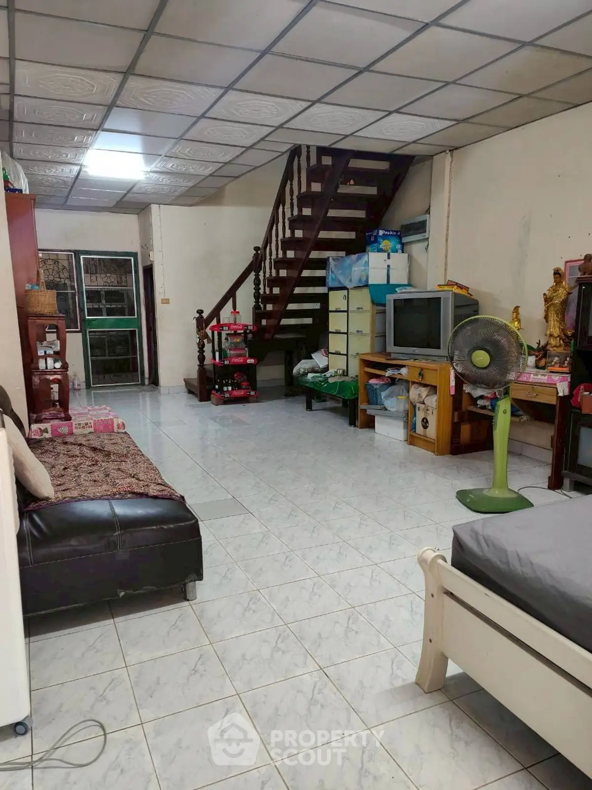 Spacious living room with tiled floor, staircase, and vintage TV setup.